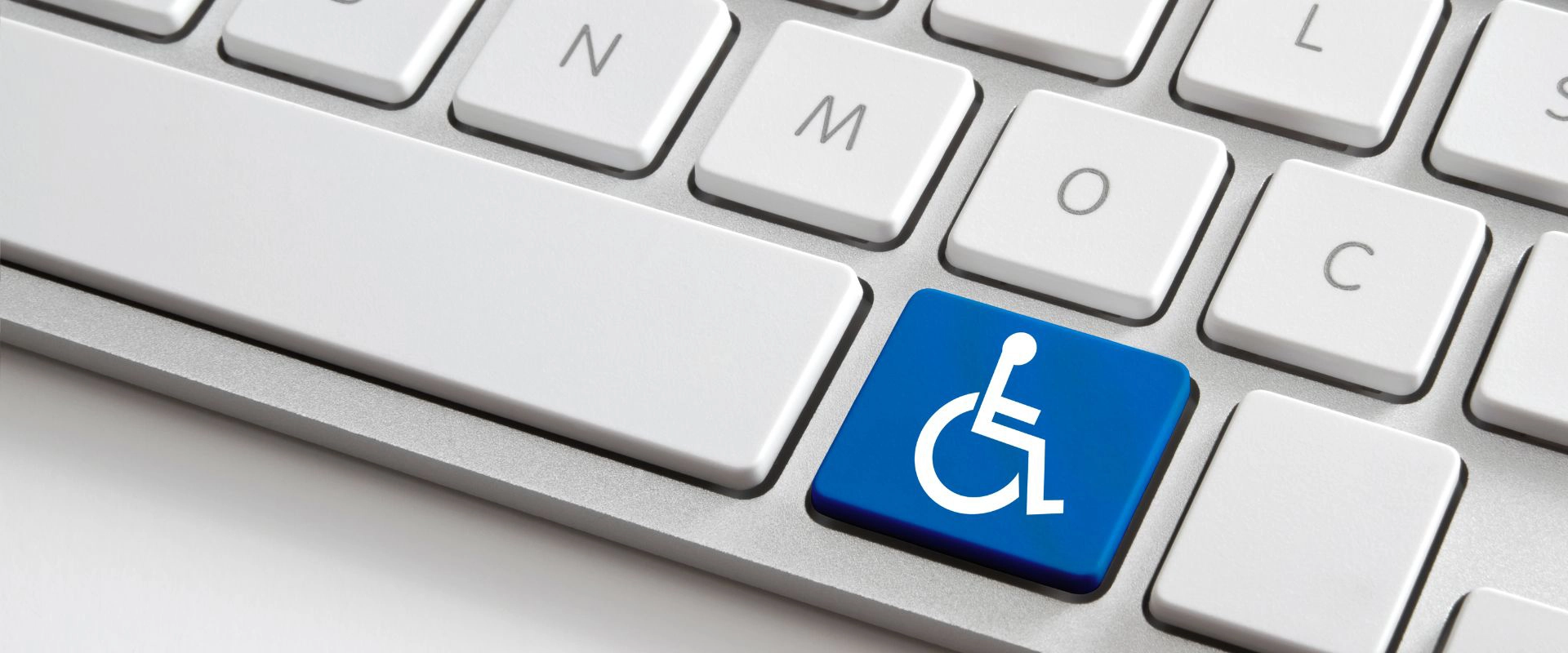 In the image there is a white keyboard. One of the keys has been replaced with a blue key with an icon of a disabled person inside.